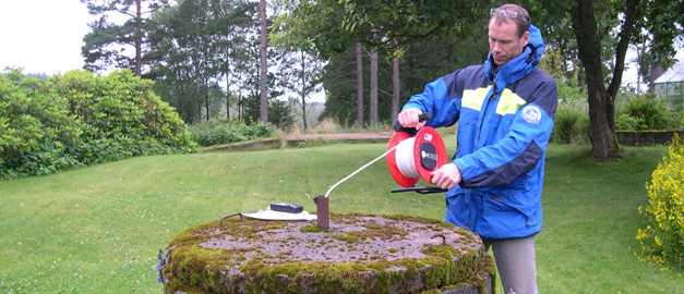 En man mäter grundvattennivån i en brunn. Han får den till 3,44 meter under röröverkant. En man mäter grundvattennivån i en brunn. Han får den till 3,44 meter under röröverkant.